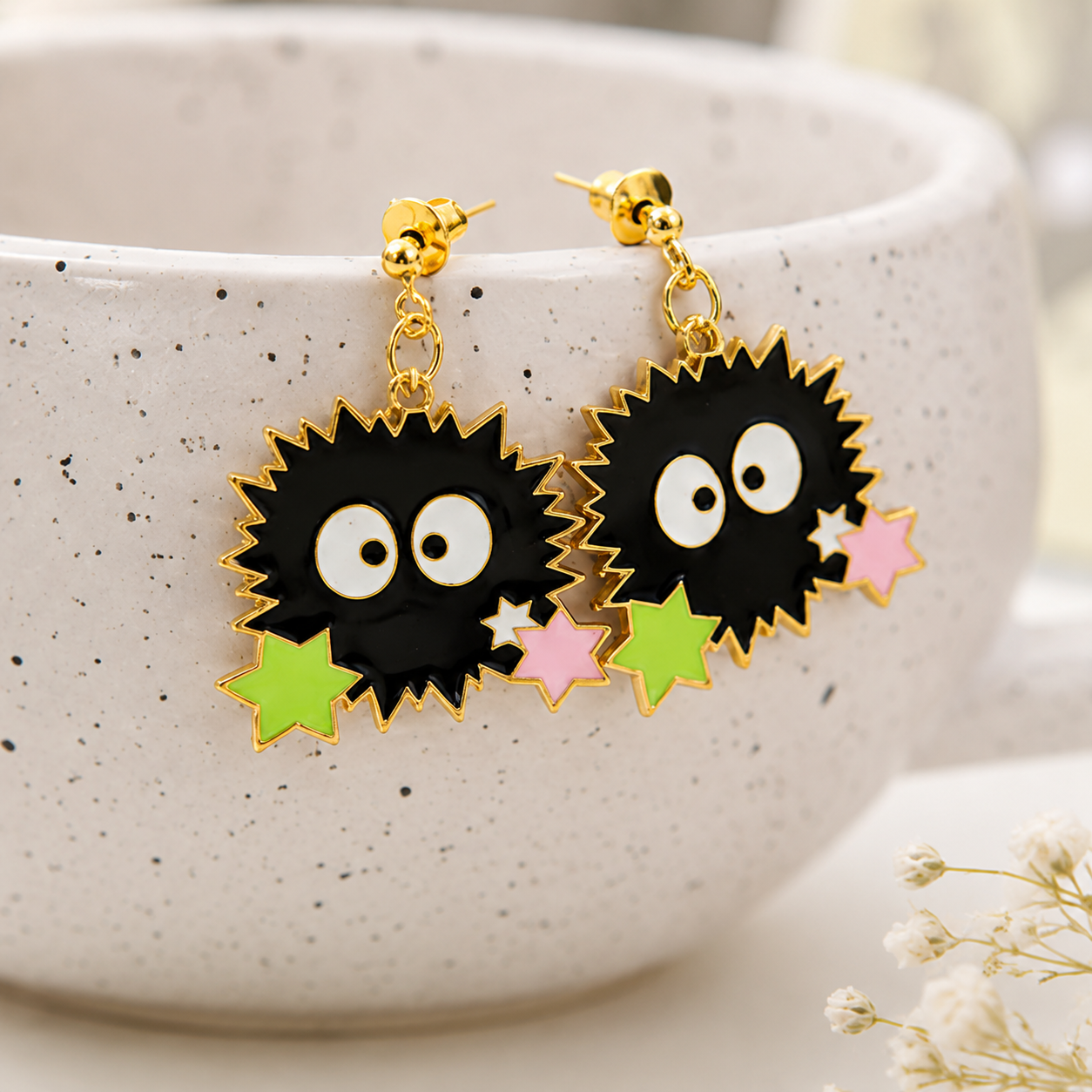 une paire de boucles d'oreilles en forme de noiraudes, ces petits êtres qui ressemblent à des boules de suie. Elles sont accompagnées de petites étoiles qui rappellent les sucreries dont elles raffolent.