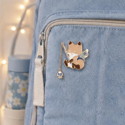 un pin's en forme de renard qui est en train de pêcher. Il a une canne à pêche composée d'une chainette. Au bout se trouve un poisson !