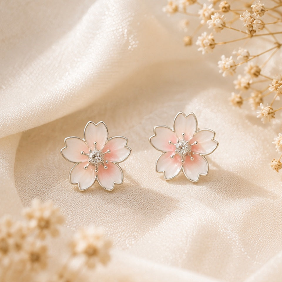 Une paire de puces d'oreilles argentées  délicates en forme de fleurs de cerisier dont le coeur est un petit strass brillant. Leur coloris rosé est délicate