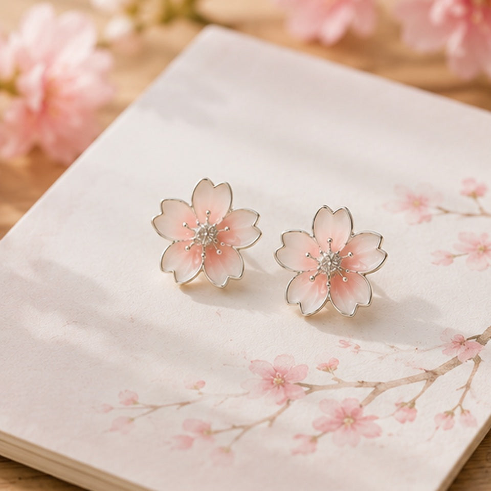 Une paire de puces d'oreilles argentées  délicates en forme de fleurs de cerisier dont le coeur est un petit strass brillant. Leur coloris rosé est délicate
