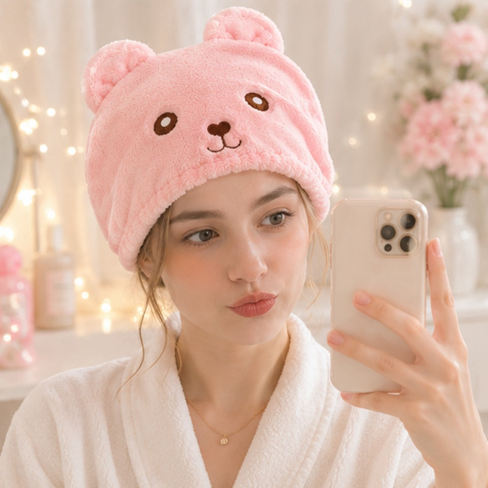 Personne portant une serviette pour cheveux kawaii rose en forme d’ourson ultra douce et moelleuse ✨ Serviette adorable avec petites oreilles et visage brodé, parfaite pour sécher les cheveux après la douche tout en ajoutant une touche cute et cosy à sa routine beauté. Ambiance cocooning pastel avec lumières chaleureuses et décoration mignonne.