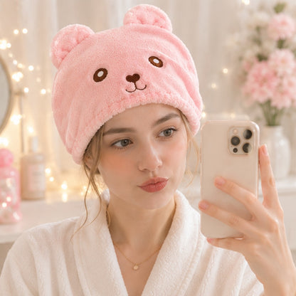 Personne portant une serviette pour cheveux kawaii rose en forme d’ourson ultra douce et moelleuse ✨ Serviette adorable avec petites oreilles et visage brodé, parfaite pour sécher les cheveux après la douche tout en ajoutant une touche cute et cosy à sa routine beauté. Ambiance cocooning pastel avec lumières chaleureuses et décoration mignonne.