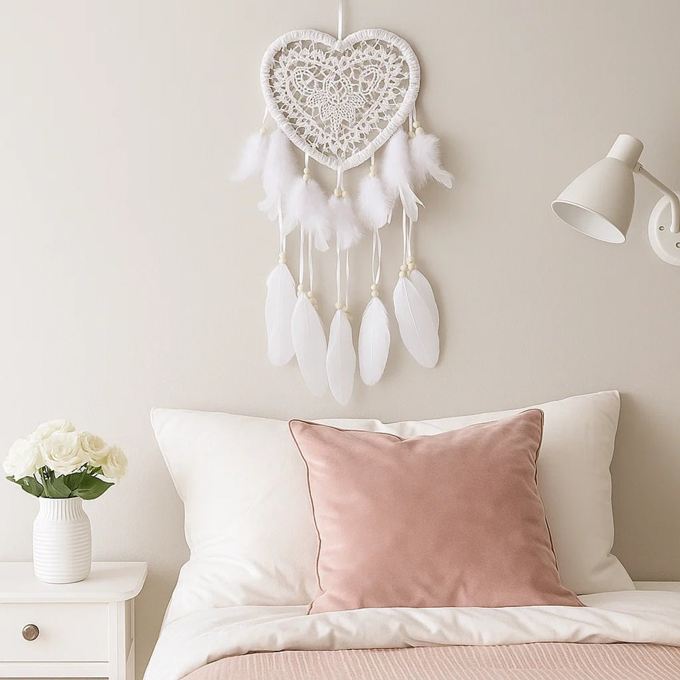 un attrape-rêves en forme de coeur tout en dentelle d'où sont suspendus des plumes blanches et des perles en bois. l'ensemble est poétique, de style bohème et léger.