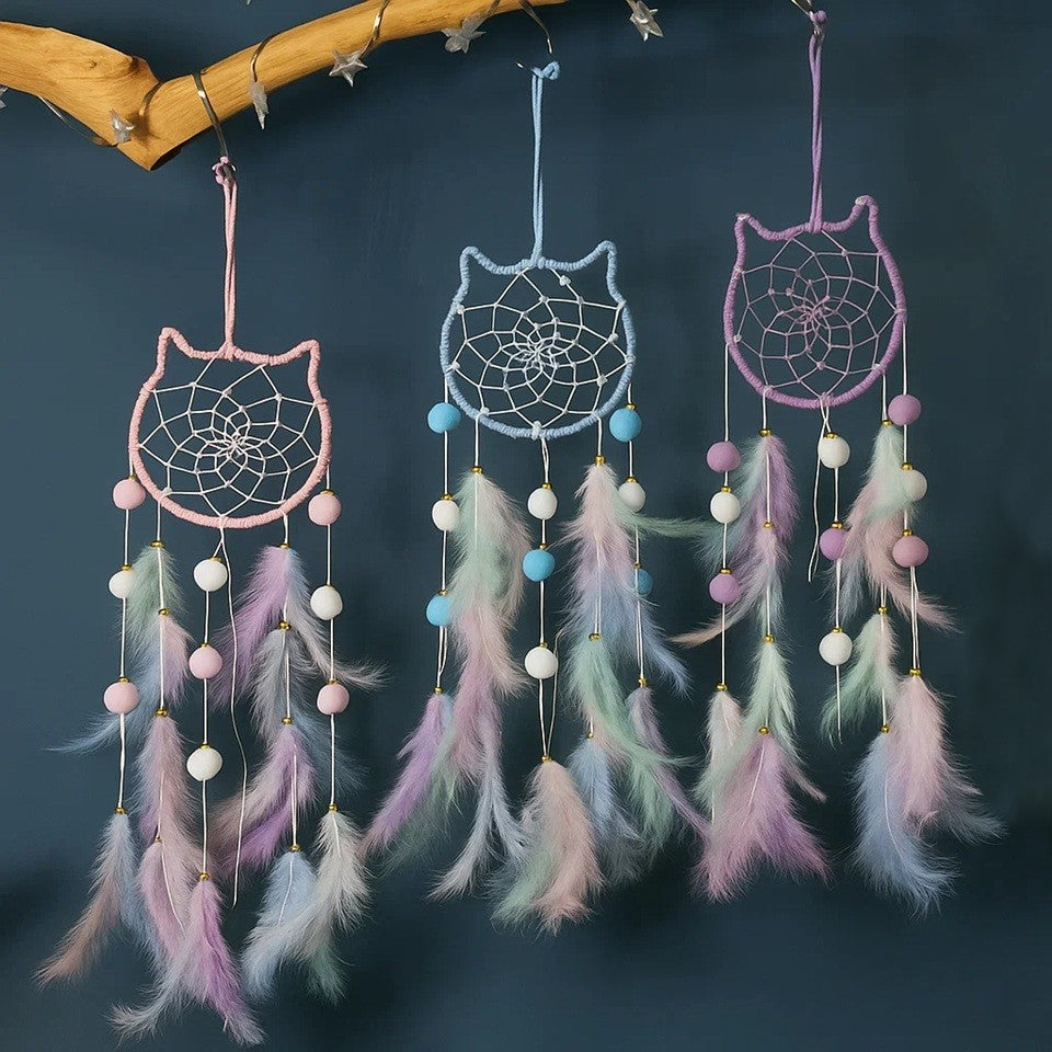 un superbe attrape-rêves en forme de tête de chat tout mignon. A l'intérieur, il y a des perles blanches dans le cordage. Des pompons et des plumes colorés y sont suspendus. L'ensemble est de couleur pastel dans un style poétique, bohême.