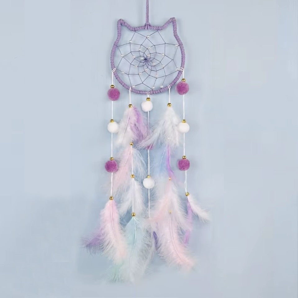 un superbe attrape-rêves en forme de tête de chat tout mignon. A l'intérieur, il y a des perles blanches dans le cordage. Des pompons et des plumes colorés y sont suspendus. L'ensemble est de couleur pastel dans un style poétique, bohême.
