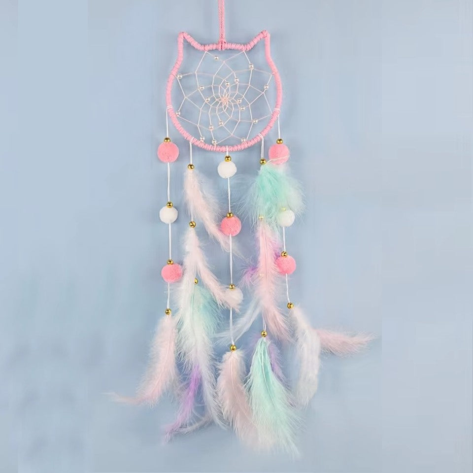 un superbe attrape-rêves en forme de tête de chat tout mignon. A l'intérieur, il y a des perles blanches dans le cordage. Des pompons et des plumes colorés y sont suspendus. L'ensemble est de couleur pastel dans un style poétique, bohême.