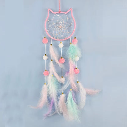 un superbe attrape-rêves en forme de tête de chat tout mignon. A l'intérieur, il y a des perles blanches dans le cordage. Des pompons et des plumes colorés y sont suspendus. L'ensemble est de couleur pastel dans un style poétique, bohême.
