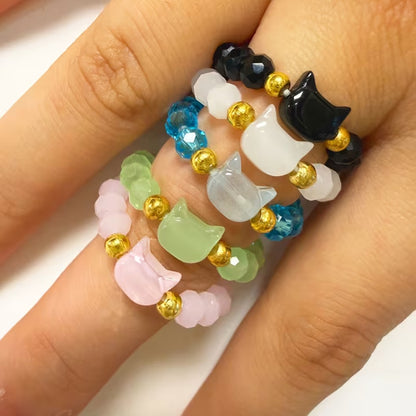 une bague taille élastique toute en parles et une breloque perles en forme de tête de chat. Disponible en coloris noir, blanc, bleu, vert, rose
