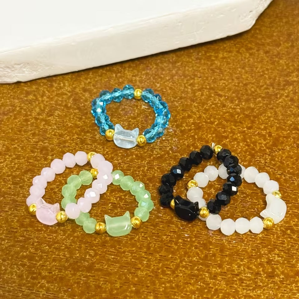 une bague taille élastique toute en parles et une breloque perles en forme de tête de chat. Disponible en coloris noir, blanc, bleu, vert, rose