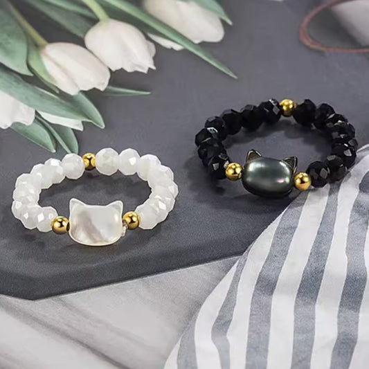 une bague taille élastique toute en parles et une breloque perles en forme de tête de chat. Disponible en coloris noir ou blanc.
