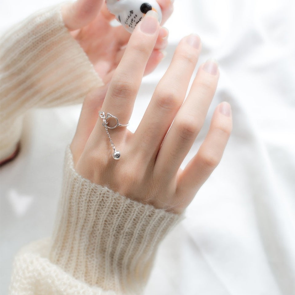 une bague argentée de taille réglable qui forme une tête de chat dans laquelle passe un petit grelot.