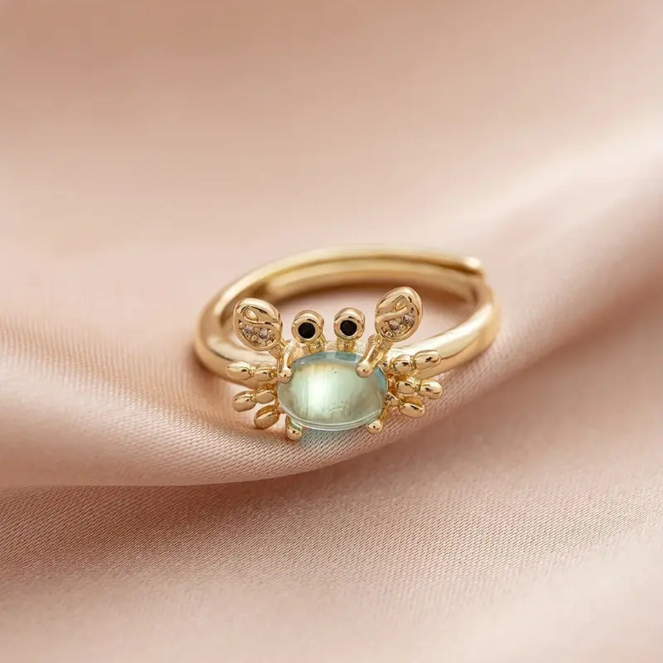 une superbe bague dorée réglable en forme de crabe qui lève les pinces. Son corps est un joli strass bleu transparent qui rappelle la mer. Ses pinces ont des strass.