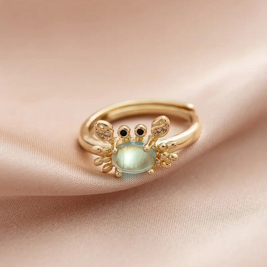 une superbe bague dorée réglable en forme de crabe qui lève les pinces. Son corps est un joli strass bleu transparent qui rappelle la mer. Ses pinces ont des strass.