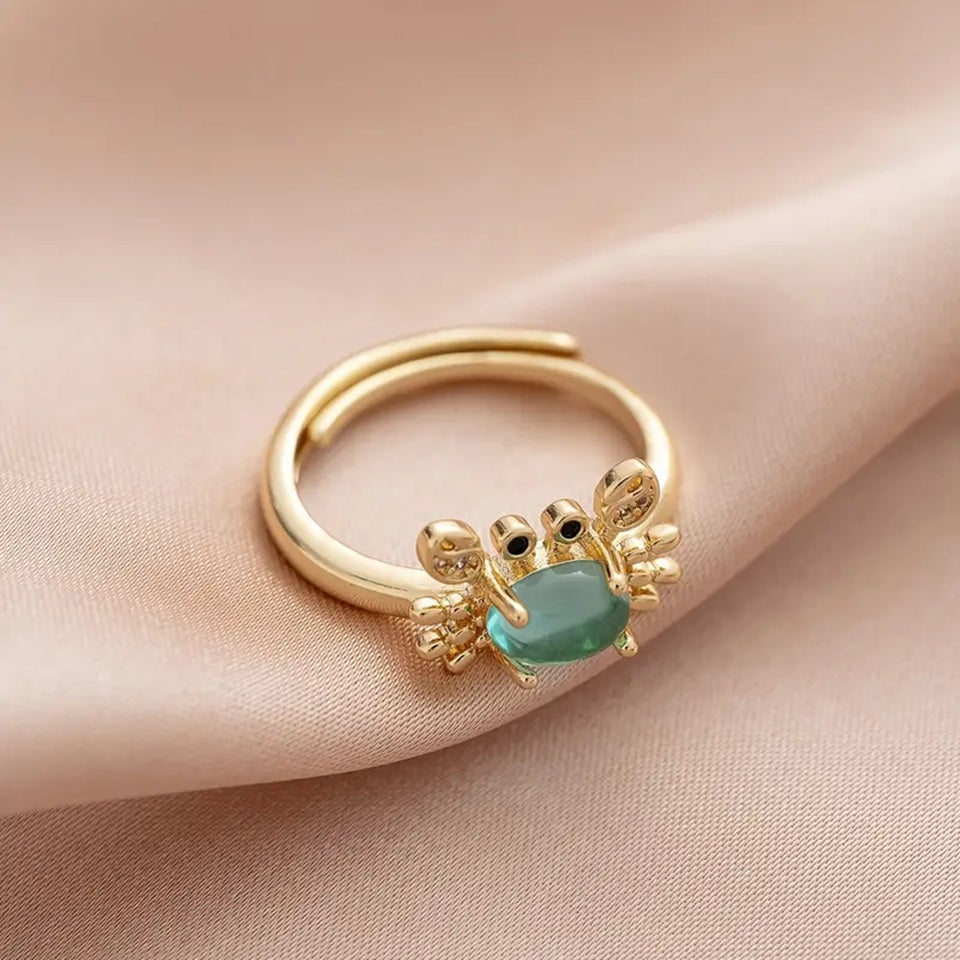 une superbe bague dorée réglable en forme de crabe qui lève les pinces. Son corps est un joli strass bleu transparent qui rappelle la mer. Ses pinces ont des strass.