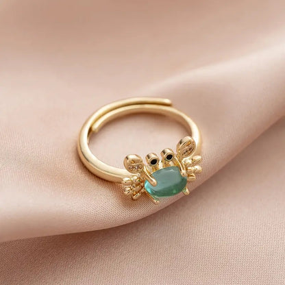 une superbe bague dorée réglable en forme de crabe qui lève les pinces. Son corps est un joli strass bleu transparent qui rappelle la mer. Ses pinces ont des strass.