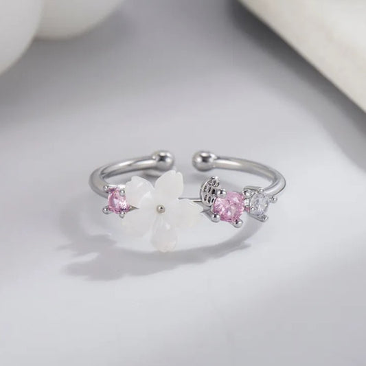 une superbe bague argentée et réglable d'une fleur de sakura blanche accompagnée de petits strass roses et blancs.