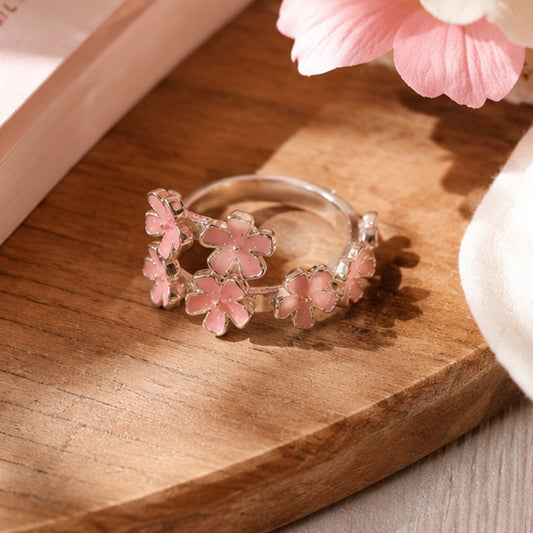 une jolie bague argentée composée de sept petites fleurs de sakura rose qui se suivent comme une farandole. Design romantique, floral et poétique.