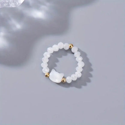 une bague taille élastique toute en parles et une breloque perles en forme de tête de chat. Disponible en coloris noir ou blanc.