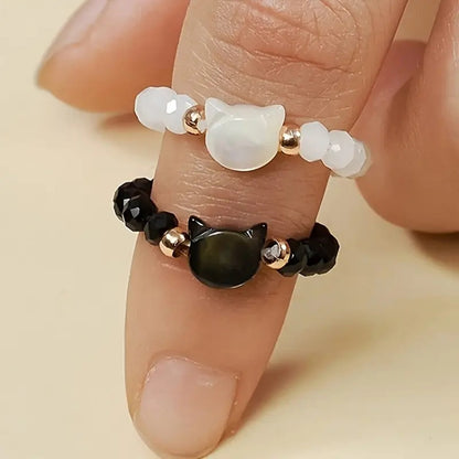 une bague taille élastique toute en parles et une breloque perles en forme de tête de chat. Disponible en coloris noir ou blanc.