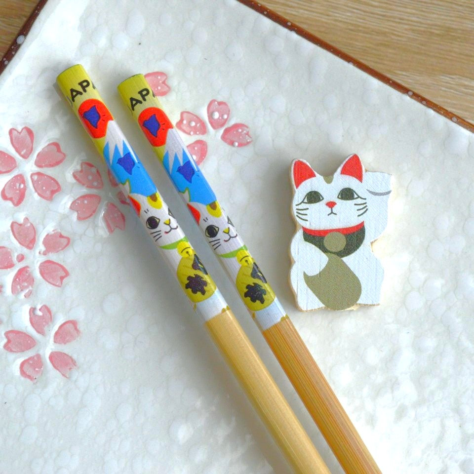 une paire de baguettes japonaises en bambou décorées d'un maneki neko et du mont fuji. Elles ont un support pour baguettes en forme d'un maneki neko blanc.