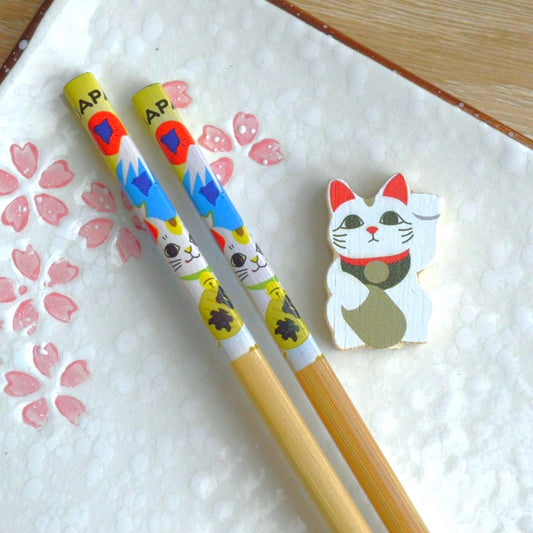 une paire de baguettes japonaises en bambou décorées d'un maneki neko et du mont fuji. Elles ont un support pour baguettes en forme d'un maneki neko blanc.