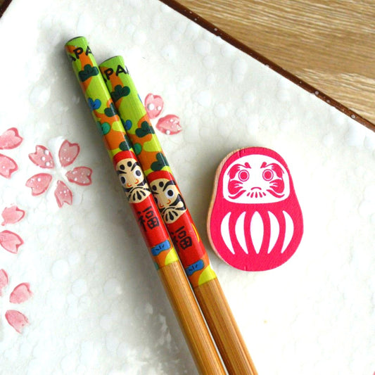 une paire de baguettes japonaises décorées d'un daruma rouge avec son repose baguette en forme de daruma. Folklore et style se combinent pour une jolie table inspiré du Japon.