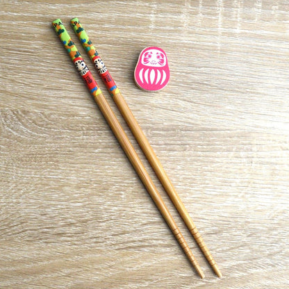 une paire de baguettes japonaises décorées d'un daruma rouge avec son repose baguette en forme de daruma. Folklore et style se combinent pour une jolie table inspiré du Japon.