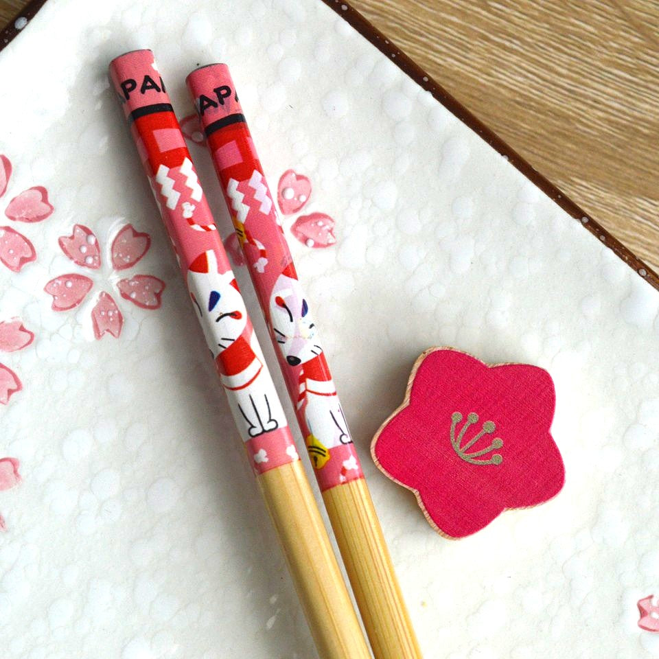 une paire de baguettes japonaises en bambou décoré d'un mignon kitsune et son repose baguette en forme de fleur de sakura rouge. Elégance et folklore japonais réunis pour une table élégante.