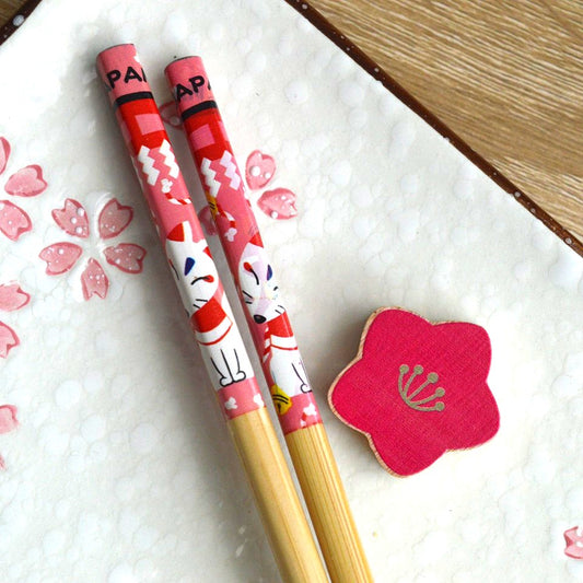 une paire de baguettes japonaises en bambou décoré d'un mignon kitsune et son repose baguette en forme de fleur de sakura rouge. Elégance et folklore japonais réunis pour une table élégante.