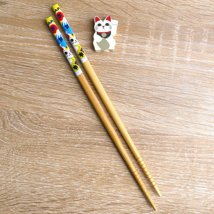une paire de baguettes japonaises en bambou décorées d'un maneki neko et du mont fuji. Elles ont un support pour baguettes en forme d'un maneki neko blanc.