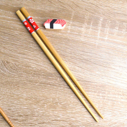 une paire de baguettes japonaises en bambou durable décorées de fleurs blanches sur un fond rouge. Elles ont un support pour baguettes en forme de sushi au thon