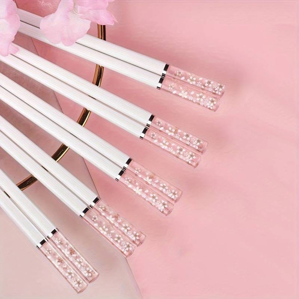 une paire de baguettes japonaises blanches délicatement décorées au bout de fleurs de sakura. Au bout, elles sont transparentes et joliment colorées de rose. Idéales pour une table élégante et raffinée.