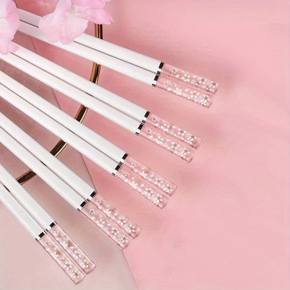 une paire de baguettes japonaises blanches délicatement décorées au bout de fleurs de sakura. Au bout, elles sont transparentes et joliment colorées de rose. Idéales pour une table élégante et raffinée.