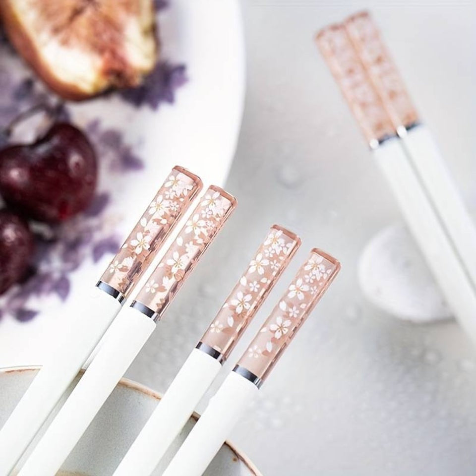 une paire de baguettes japonaises blanches délicatement décorées au bout de fleurs de sakura. Au bout, elles sont transparentes et joliment colorées de rose. Idéales pour une table élégante et raffinée.