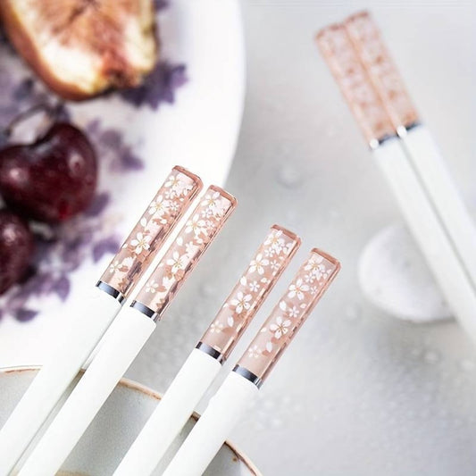 une paire de baguettes japonaises blanches délicatement décorées au bout de fleurs de sakura. Au bout, elles sont transparentes et joliment colorées de rose. Idéales pour une table élégante et raffinée.