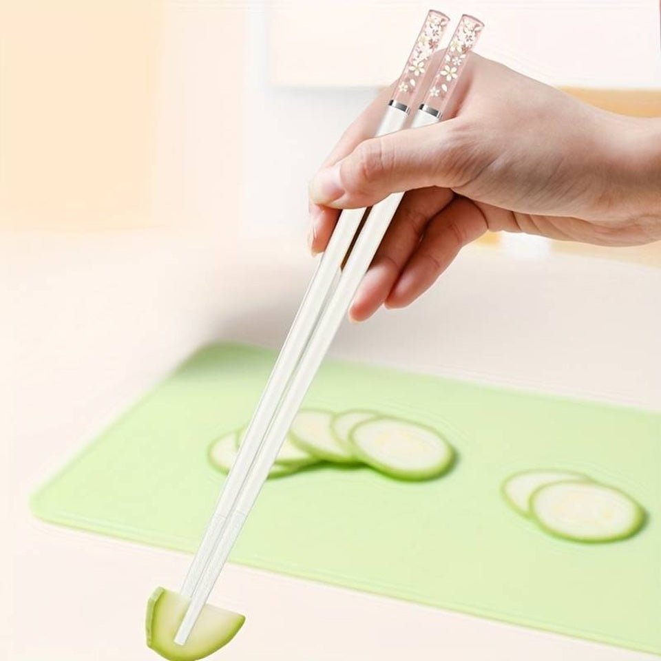 une paire de baguettes japonaises blanches délicatement décorées au bout de fleurs de sakura. Au bout, elles sont transparentes et joliment colorées de rose. Idéales pour une table élégante et raffinée.
