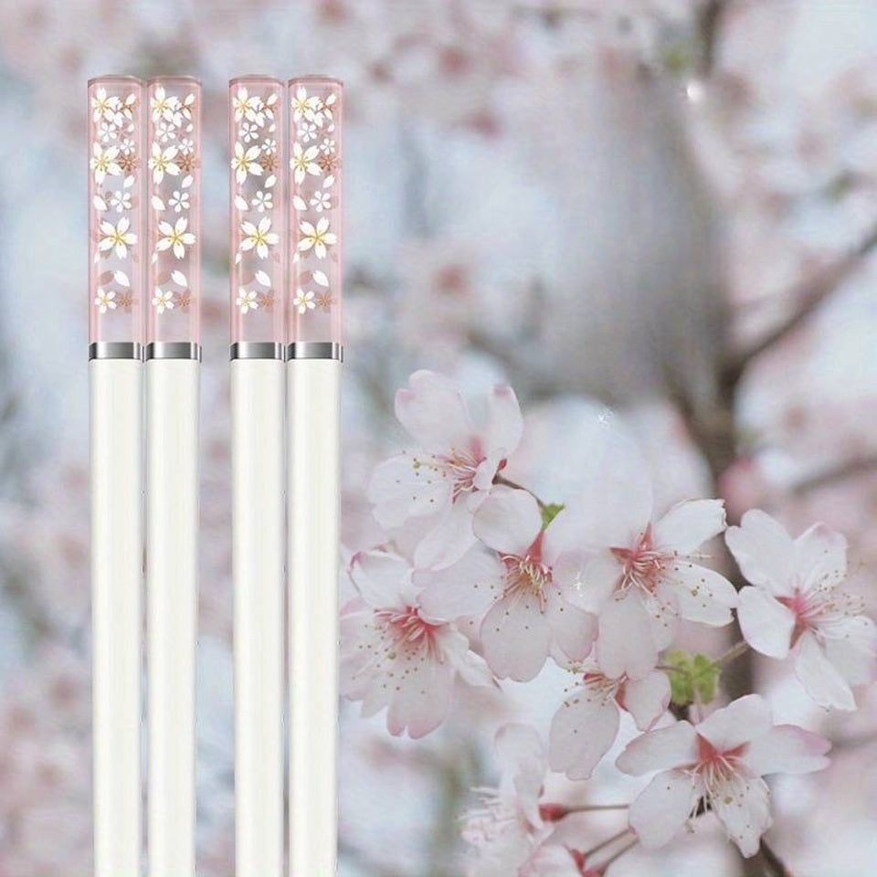 une paire de baguettes japonaises blanches délicatement décorées au bout de fleurs de sakura. Au bout, elles sont transparentes et joliment colorées de rose. Idéales pour une table élégante et raffinée.