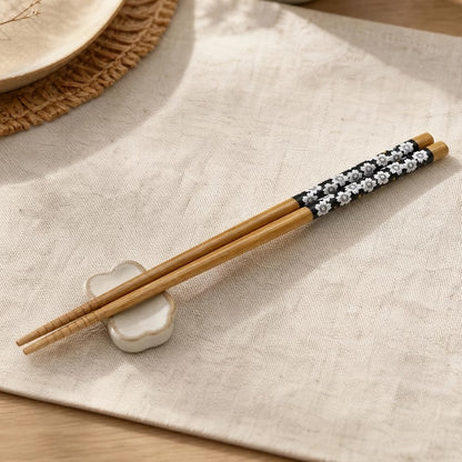 Gros plan sur une paire de baguettes en bambou noir au motif de fleurs de sakura du Japon. Joliment posées sur un chemin de table en lin, elles sont parfaites pour un repas calme et serein.
