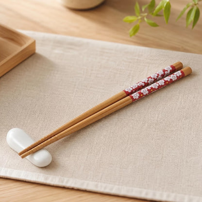 Gros plan sur une paire de baguettes en bambou rouge au motif de fleurs de sakura du Japon. Joliment posées sur un chemin de table en lin, elles sont parfaites pour un repas calme et serein.