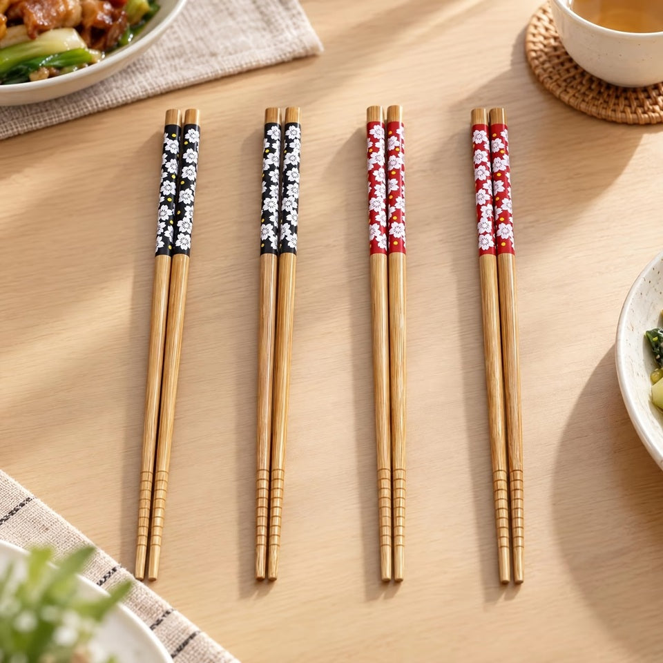 Des paires de baguettes en bambou, une noire et une rouge, au motif de fleurs de sakura du Japon posées sur une jolie table. Ambiance zen, calme qui rappelle le Japon.