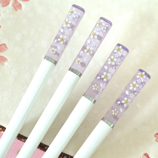 une paire de baguettes japonaises blanches dont le bout est transparent et violet et est décoré de jolies fleurs de sakura blanches