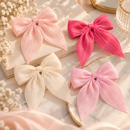 Barrettes à cheveux en forme de nœud rose, fuchsia et blanc avec fins fils dorés, présentées dans un décor romantique, doux et élégant.
