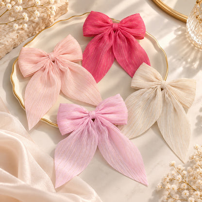 Barrettes à cheveux en forme de nœud coloré rose, fuchsia et blanc, ornées de fins fils dorés, présentées dans un décor romantique et élégant.