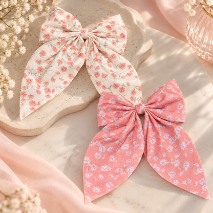 Barrettes à cheveux en forme de nœud fleuri rose et écru, ornées de petites fleurs, présentées dans un décor romantique et délicat.