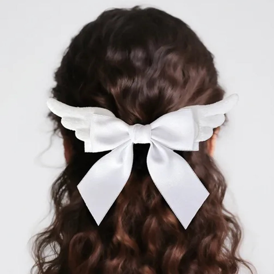 Une barrette à cheveux en forme de nœud avec ailes blanches, portée dans les cheveux par une femme brune. Un accessoire élégant et romantique qui apporte une touche poétique et féminine.