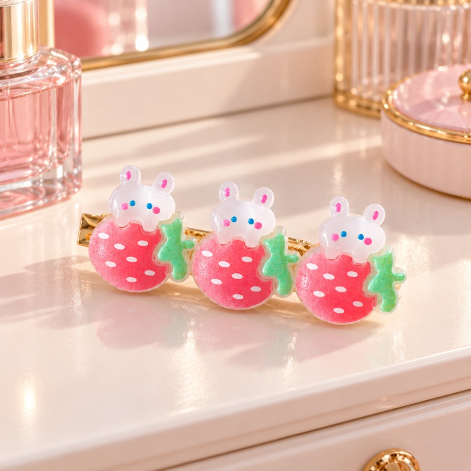 Barrette à cheveux kawaii ornée de trois adorables lapins blancs aux joues roses, posés sur des fraises roses à pois blancs et feuilles vertes. Accessoire pour cheveux mignon et original, présenté sur une coiffeuse élégante aux tons pastel, avec un flacon de parfum rose en arrière-plan.