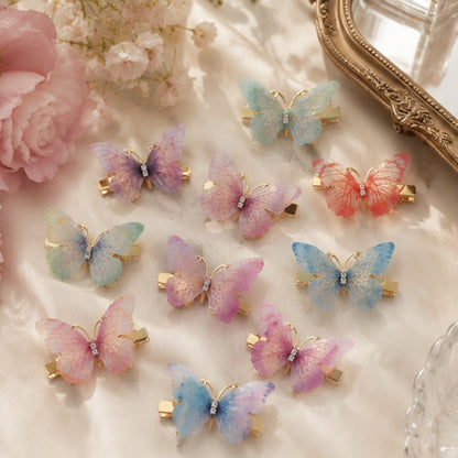des barrettes à cheveux en forme de papillons colorés posés sur une coiffeuse avec des fleurs roses et un miroir. Les ailes des papillons sont en tissu colorés et ils sont dorés.