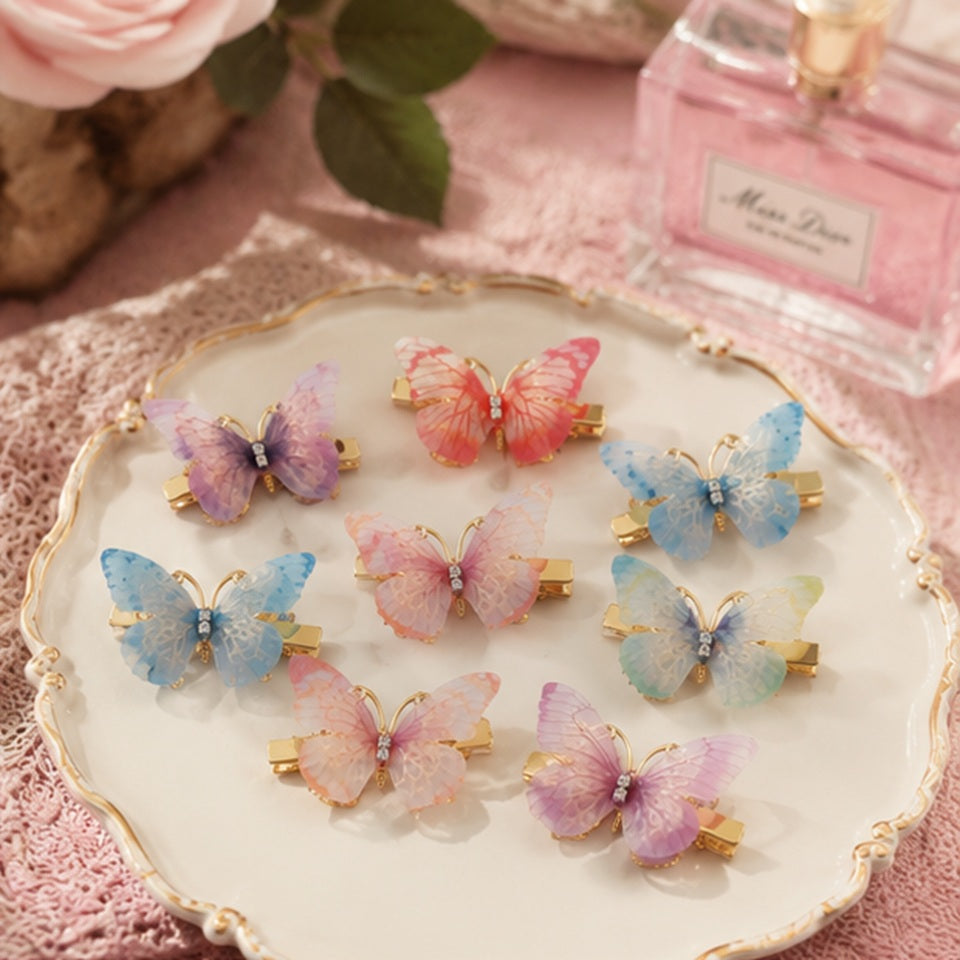 des barrettes à cheveux en forme de papillons colorés posés sur un plateau blanc et doré. Les ailes des papillons sont en tissu colorés et ils sont dorés.