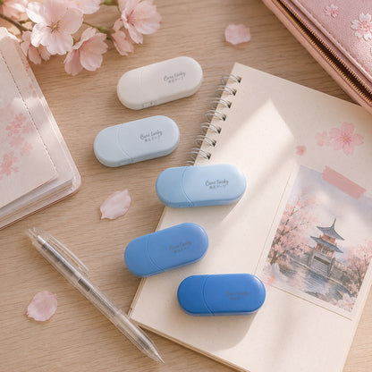 Blancos ruban correcteurs ovales en dégradé de bleu et blanc, présentés dans un joli décor de bureau avec carnet, stylo et fleurs de sakura.