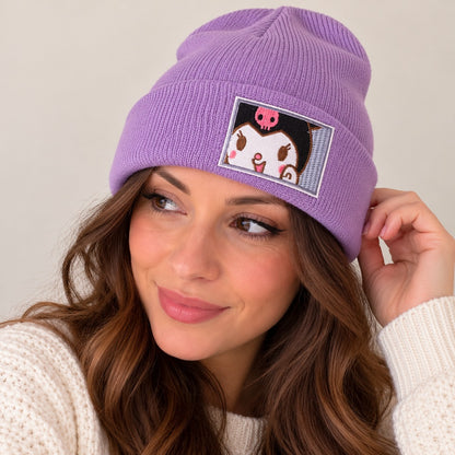Femme portant un bonnet violet lavande en maille côtelée avec broderie Kuromi, personnage kawaii Sanrio. Associé à un pull blanc, ce bonnet doux et chaud au style japonais est présenté sur un fond beige épuré, idéal pour l'automne et l'hiver.